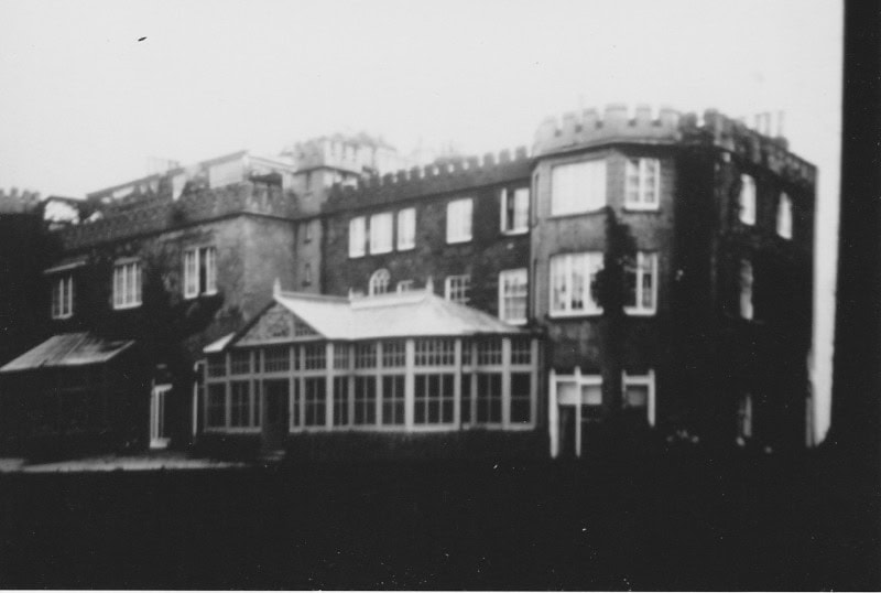 Black and white photo of a large old building with many windows and castle-like battlements on the roof.